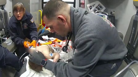 A first responder administers aid to an 11-month-old in the back of an ambulance