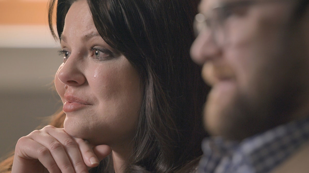 A close-up of Amy Duggar King crying sitting next to her husband.