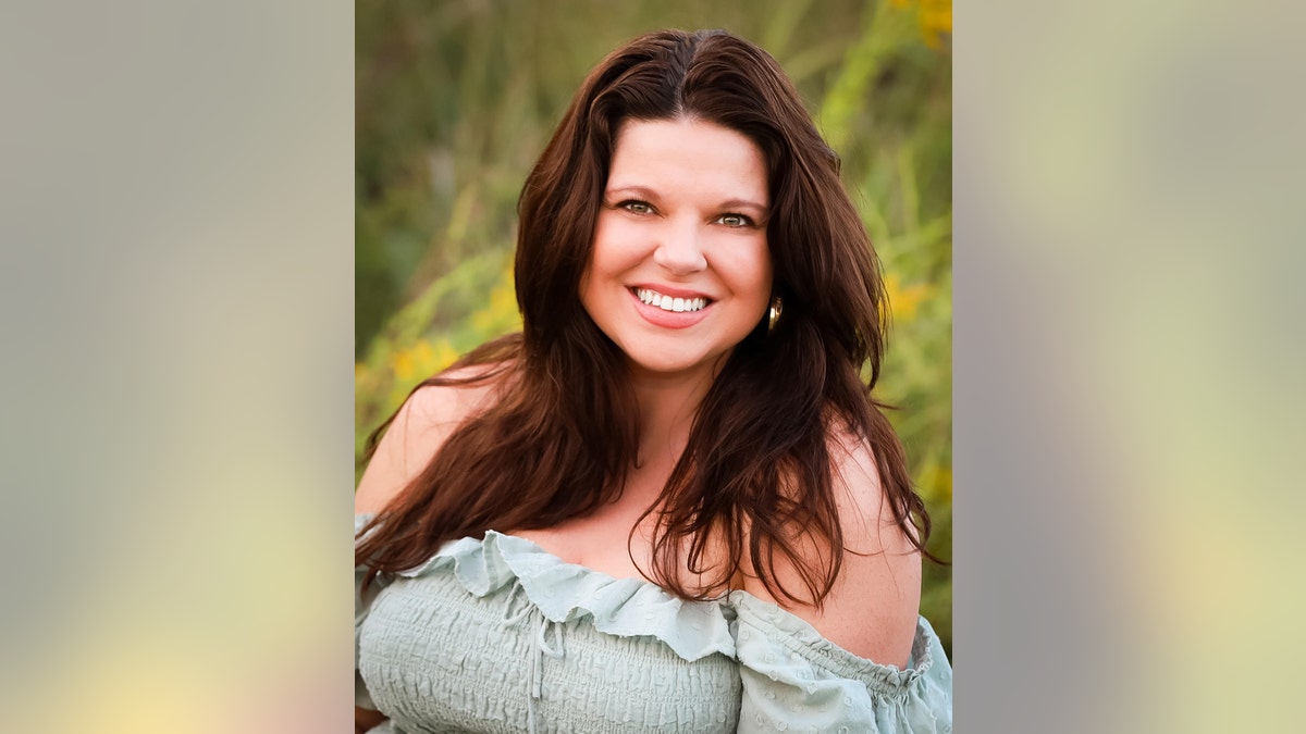 A close-up of Amy Duggar King smiling with an off the shoulder light green dress in a field.