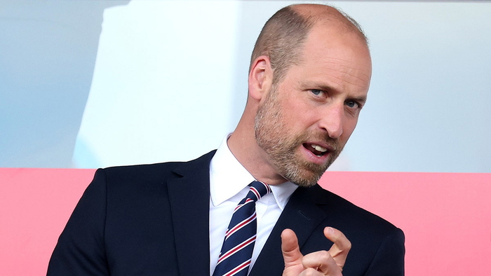 El príncipe William en medio de la conversación vistiendo un blazer negro y una corbata a rayas.