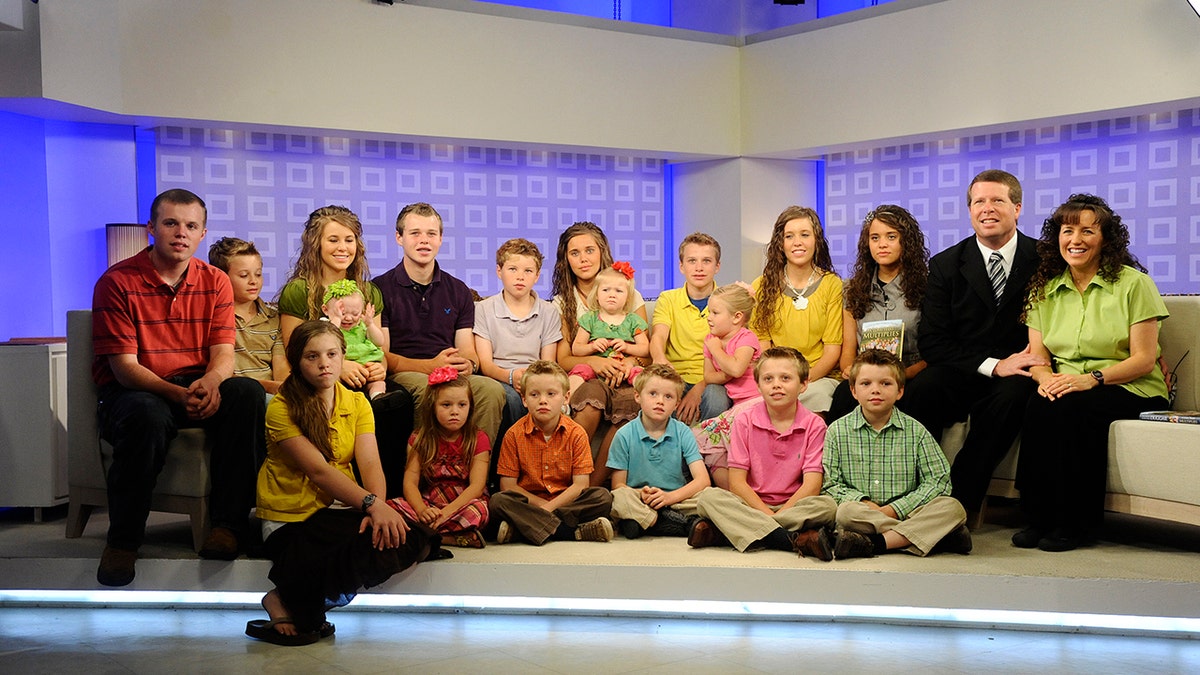 The cast of 19 kids and counting sitting together and smiling.