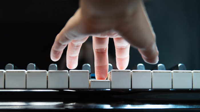 Una mano sobre el teclado de un piano, pulsando una tecla con el dedo corazón