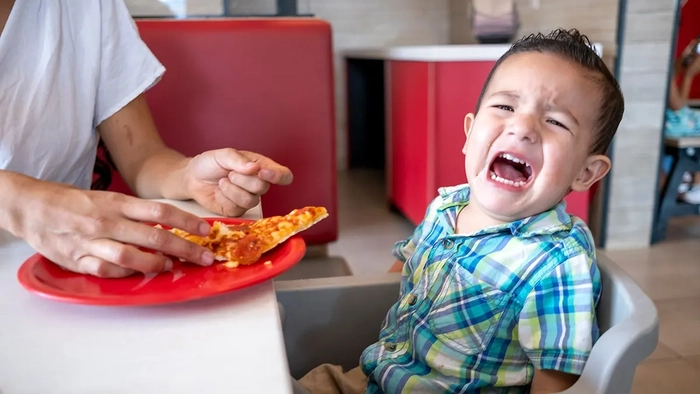 ¿Harto de niños gritones en la cena? Más estadounidenses apoyan las cenas sólo para adultos Un niño pequeño con una rabieta dentro de un restaurante al ver una pizza.