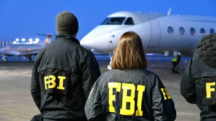 El FBI captura a un fugitivo bangladeshí extraditado por un caso masivo de extorsión sexual infantil en Internet Agentes del FBI parados en la pista de un aeropuerto cerca de un jet privado por la noche.