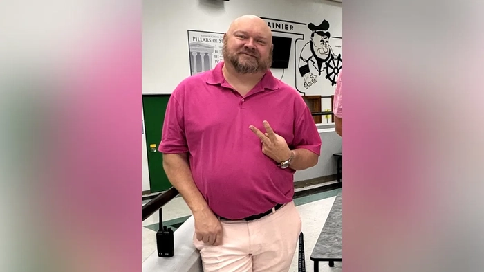 Бывший директор школы Джереми П. Уильямс позирует для фото, держа в руках знак мира.