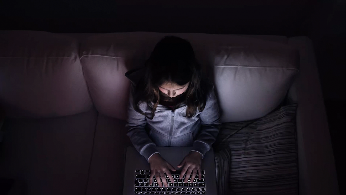 Niña pequeña, sentada en la oscuridad, jugando con la computadora portátil .