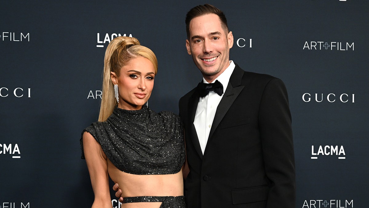 Paris Hilton con un vestido recortado brillante con el pelo recogido posa con su esposo Carter Reum con un esmoquin clásico en la alfombra