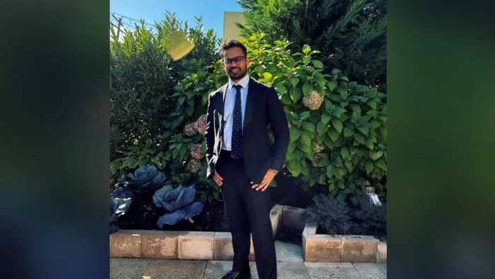 Таухид Дьюан стоит в костюме и улыбается на фоне природы