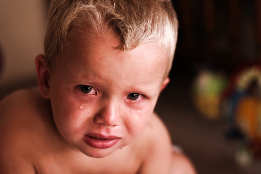 Photograph of a shirtless child with tears in his eyes looking sadly.