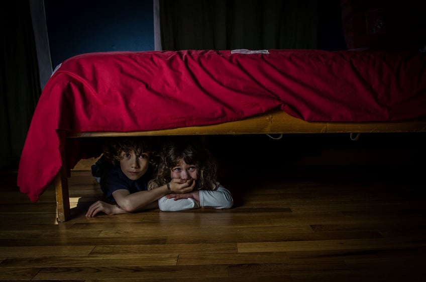 Dos niños asustados escondiendose debajo de una cama.