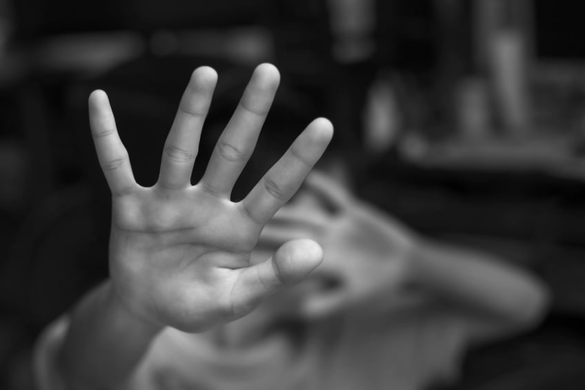 Una foto en blanco y negro que muestra a un niño asustado extendiendo defensivamente los brazos y las manos.