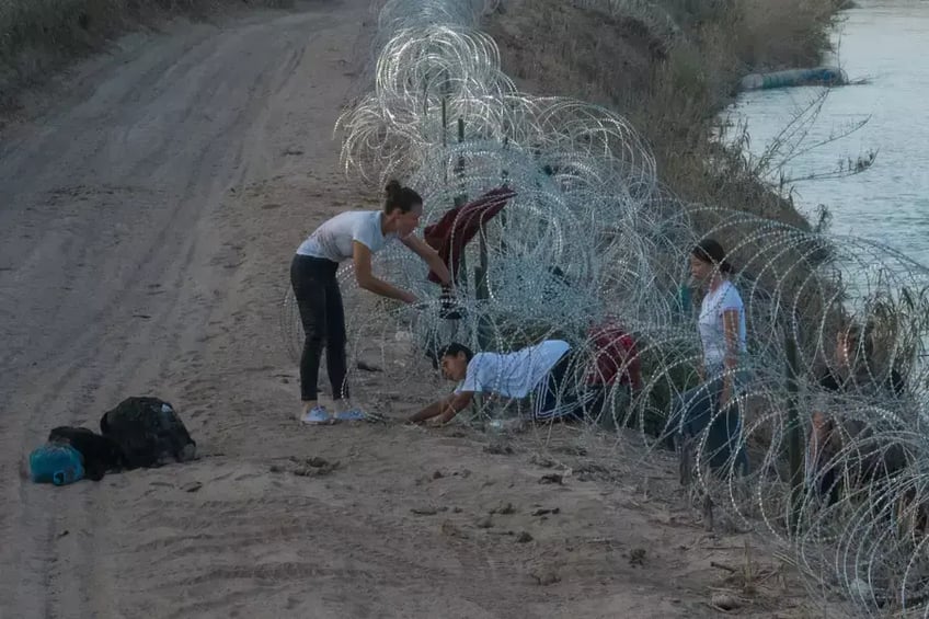 People trying to cross the border into the United States between the barbed wire.