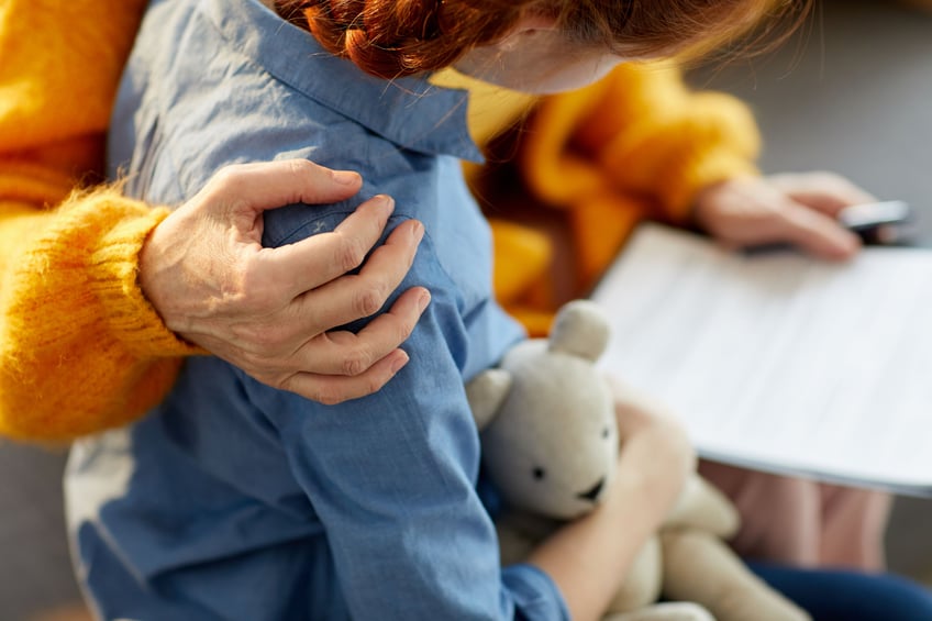 Girl hugging a teddy bear together with an adult reading a document.